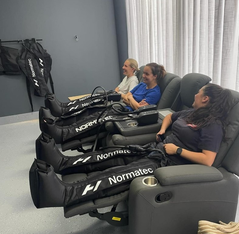 Three people relaxing in recliners wearing Normatec compression boots at Revive Hub